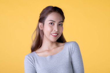 Sarı arka planda dikilip kameraya bakan sıradan giyinmiş güzel, gülümseyen Asyalı bir kadının portresi.