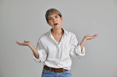 Kafası karışmış orta yaşlı Asyalı kadının görüntüsü beyaz arka planda tek başına duruyor. Kameraya bak.