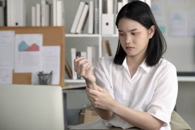 Bilgisayarda çalışırken bilek ağrısı çeken genç Asyalı iş kadını, bilgisayarın önünde uzun saatler geçirdikten sonra el ve bileğine masaj yapan iş kadını, Sağlık Bakanlığı sendromu konsepti.