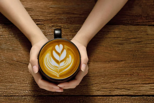 Mujer sosteniendo taza de café con leche en la mesa de madera —  Fotos de Stock