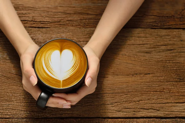 Mulher segurando xícara de café latte, com forma de coração — Fotografia de Stock