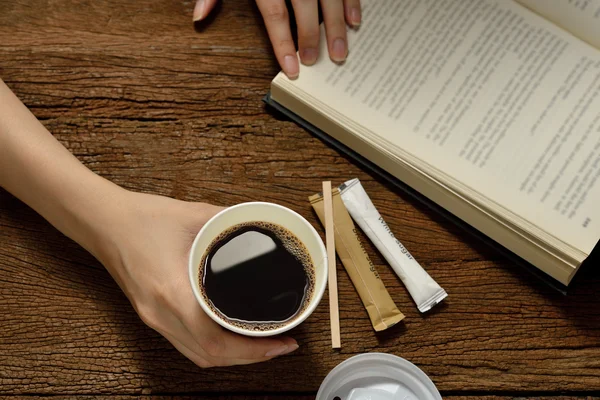 女人抱着纸杯装的咖啡和木制的桌子上读书 — 图库照片