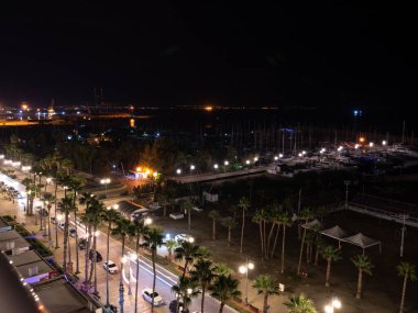 Kıbrıs Rum Kesimi 'nin Larnaka kentindeki Akdeniz kıyısında yatları olan Finikoudes Palmiye ağaçlarına tepeden bakan gökyüzü manzarası. Siyah gökyüzü ve sokak lambalarıyla sanayi şehri.