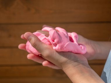 Çocuk el ele tutuşması ve kahverengi ahşap arka planda yumuşak pembe balçık sıkma.