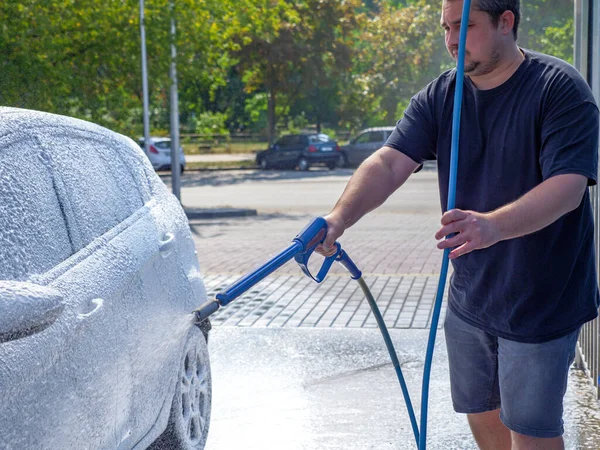 Elinde yüksek güçlü hortumlu bir adam arabasını oto yıkamada yıkıyor ve sürücü koltuğundan manzarayı seyrediyor. Kişisel temastan kaçının ve yalnız yıkayın..