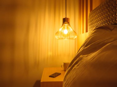 Ön planda büyük bir yastık ve arka planda telefon ve fincanı olan sarı ışıklı bulanık metal abajur. Rahatlatıcı akşam atmosferi konsepti.