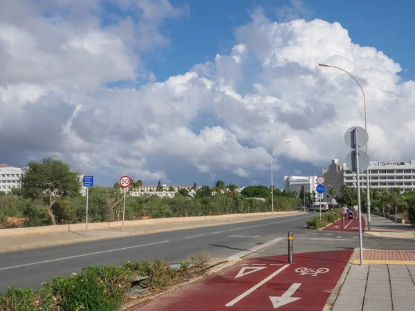 Picturesque road with cycle lanes to Ayia Napa, Cyprus. Cityscape with scenic white puffy mountain-like clouds above hotel buildings.