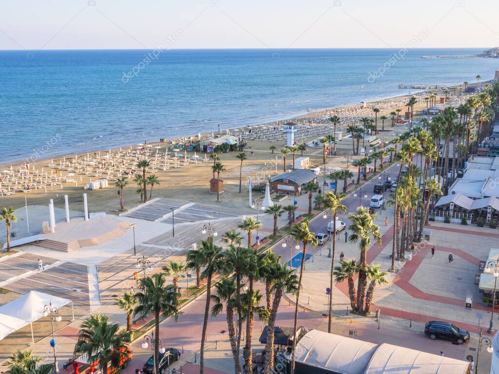 Top aerial view overlooking Finikoudes Palm tree promenade, road with cars, and central beach near the Mediterranean sea in Larnaca city, Cyprus.