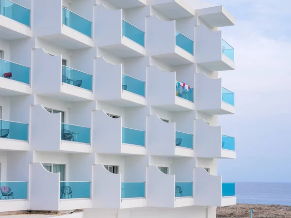 Facade of a modern building with blue transparent plastic balconies and view over the Mediterranean sea and empty rocky shore near Nissi beach. Warm autumn in Cyprus.
