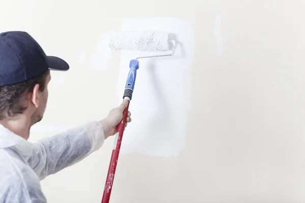 Pintor pinta parede com rolo de pintura branco — Fotografia de Stock
