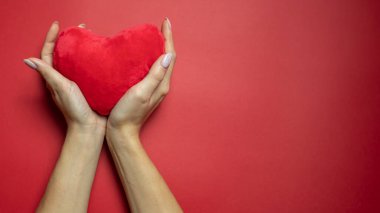 Kırmızı arka planda kırmızı kalp, kadın ellerinde. Yanlamasına. Yan görüş. Uzayı kopyala Mesajın için yer aç. 14 Şubat. Sevgililer Günü..