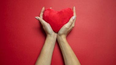 Kırmızı arka planda kırmızı kalp, kadın ellerinde. Görüntüyü ortala Uzayı kopyala Mesajın için yer aç. 14 Şubat. Sevgililer Günü..