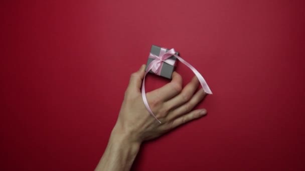Αρσενικό χέρι περνά ένα δώρο στο θηλυκό χέρι σε κόκκινο φόντο. — Αρχείο Βίντεο