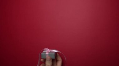 Erkek eli kırmızı arka planda bir kadına hediye verir..