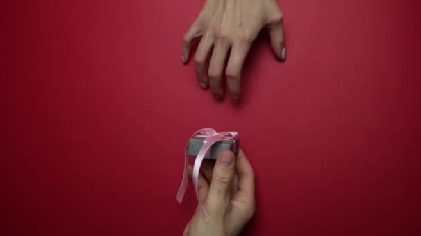 Мужская рука передает подарок женской руке на красном фоне. — стоковое видео