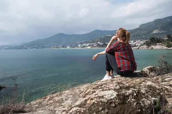 端に座って穏やかな海と島を背景に美しい自然景観を観察する若い女性 — ストック写真