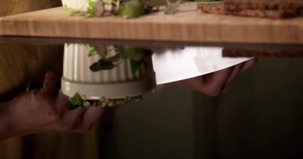 Tilt up reflection shot of woman slicing avocado on wooden cutting board — стоковое видео