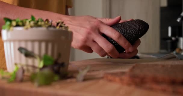 Woman slicing fresh ready-to -eat avocado to make sandwich with microgreens. — стоковое видео