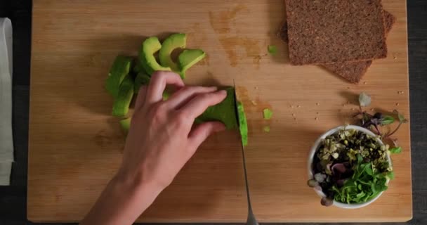 Vista dall'alto di affettare avocado fresco maturo su tagliere in legno con microverdi — Video Stock