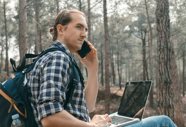 Genç Adam Ormanda Oturmuş Akıllı Telefonla Konuşuyor Dizüstü Bilgisayarla Çalışıyor — Stok fotoğraf