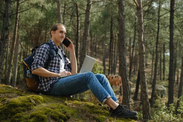 Genç Adam Ormanda Oturmuş Akıllı Telefonla Konuşuyor Dizüstü Bilgisayarla Çalışıyor — Stok fotoğraf