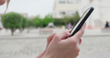 Parktaki bankta oturan akıllı telefonlu genç bir kadın.