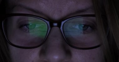 Gözlüklü kız karanlık bir odada bilgisayar kullanıyor.