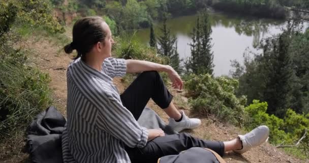 Muž Turista Klobouku Sedí Svahu Obdivuje Scenérie Lesní Rybník — Stock video