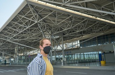 Havaalanında siyah koruyucu yüz maskesi takan genç bir turist. Seyahat için yeni normal