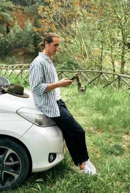 Doğada akıllı telefonunu kullanan bir adam seyahat sırasında canlı yayın izliyor. Adam elinde telefonla ekrana bakıyor. Sosyal medya videosu içeriğini izliyor.