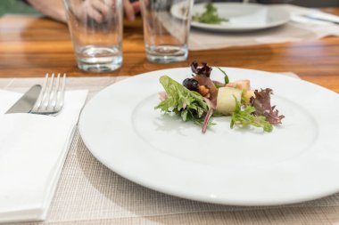 Az miktarda jambonlu salata, kavrulmuş halloumi peyniri ve ahşap masada beyaz tabakta yeşil salata.