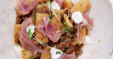 Bolonez soslu, jambonlu, taze otlu ve bir tutam ricotta peynirli lezzetli rigatoni tabağının üst görüntüsünü kapatın..
