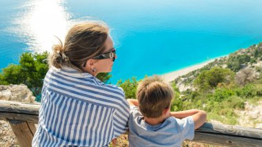 Oğluyla birlikte güzel orta yaşlı bir kadın gün batımında güzel sahil şeridini seyrediyor.. 