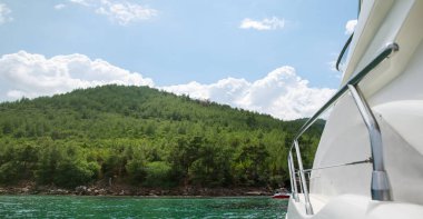 Beyaz yattan manzaralı ada manzarası. Gündüz vakti denizde lüks bir yat. Özel tekne gezisi konsepti. Ada manzarasına odaklan