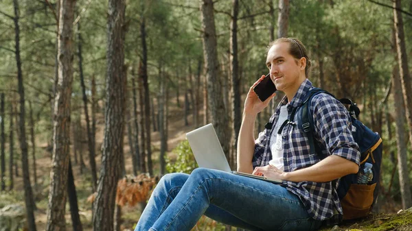 Genç Adam Ormanda Oturmuş Akıllı Telefonla Konuşuyor Dizüstü Bilgisayarla Çalışıyor — Stok fotoğraf