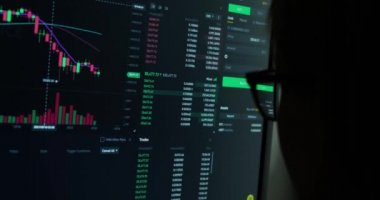 Yeşil ve kırmızı göstergeli kripto fiyatlarını canlı güncelleyen monitör, bitcoin 'in finansal tabloları, online yatırım platformu, gözlüklü kişi önde.