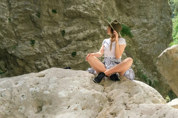 Şapkalı genç hippi kadın bir kayanın üzerinde oturuyor ve ulusal parktaki yüksek uçurumların arasında eğleniyor. Fotokopi alanı, dijital detoks ve akıl sağlığı kavramı..