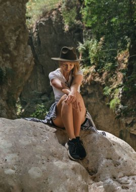 Ulusal parkta bir kayanın üzerinde oturan şapkalı genç hippi kadın dijital detoks ve akıl sağlığı kavramı..