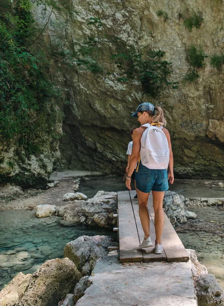 Back view of traveler woman with backpack walking across small creek. travel through scenic places, trekking, hiking, a woman walks along a tourist route, mountain road, canyon.