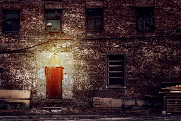 old brick building at night, dim light over the iron door. gloomy atmosphere and boarded-up windows, a criminal area