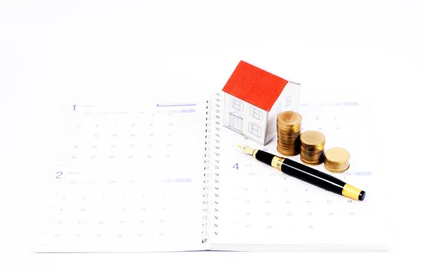 Mortgage loan planning concept with fountain pen and coins and paper house on calendar book pages