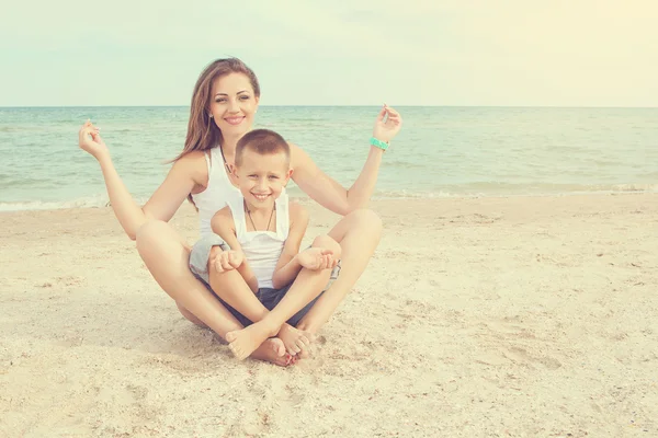 Moeder en haar zoon doet yoga op zee op strand. — Stockfoto