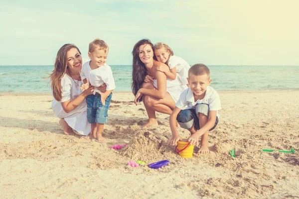 Twee jonge moeders en hun kinderen plezier op het strand — Stockfoto