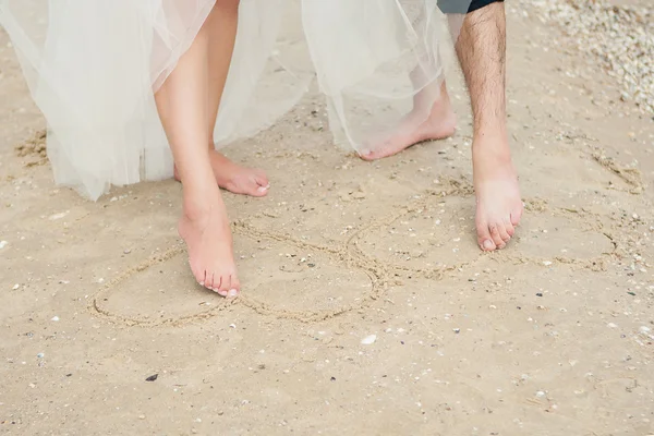 Pareja piernas pintar corazón en la arena . — Foto de Stock