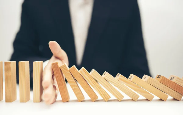 İşadamı elini kapatır, domino taşları devrilmeye devam eder.