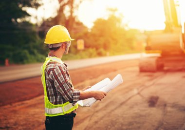 Makine geçmişi ve güvenlik kavramına sahip yol inşaatı projesini elinde tutan mühendis.