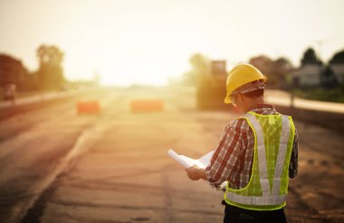 Makine geçmişi ve güvenlik kavramına sahip yol inşaatı projesini elinde tutan mühendis.
