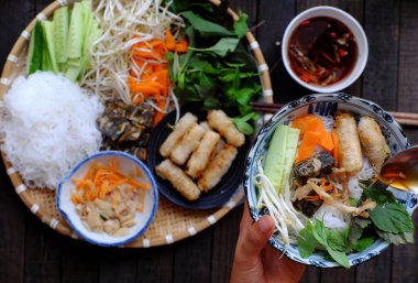 Vietnam 'da vejetaryen yemeği yiyen insanlar, pirinç eriştesi, öğle yemeği zamanında baharatlı kızarmış börek ve sos yiyen insanlar, yiyecek arka planında yakın el ele tutuştukları erişte kasesi.