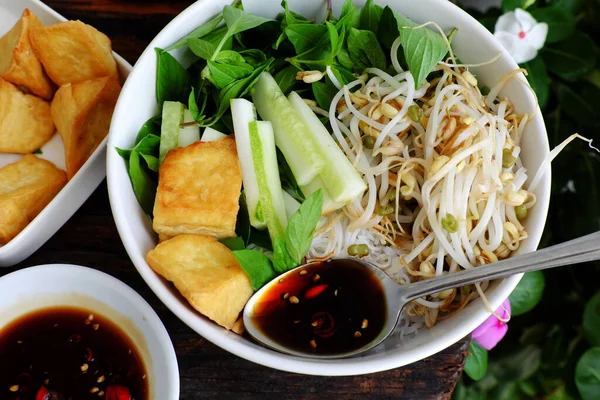 Vietnamese vegan meal for quick lunch time with homemade food, rice vermicelli soft noodles and fried tofu, cucumber, bean sprouts, soy sauce, delicious vegetarian dish on wooden background