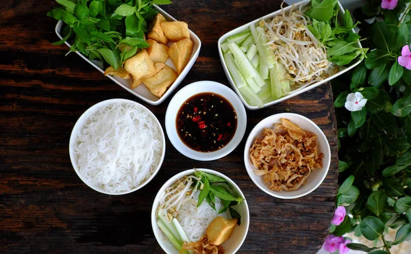 Vietnamese vegan meal for quick lunch time with homemade food, rice vermicelli soft noodles and fried tofu, cucumber, bean sprouts, soy sauce, delicious vegetarian dish on wooden background